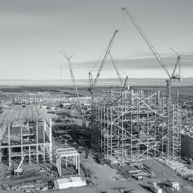 Montaje de una planta industrial en obra, con grúas de gran porte y estructura metálica.
